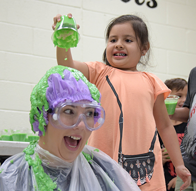 lady with green slime being poured on head by student
